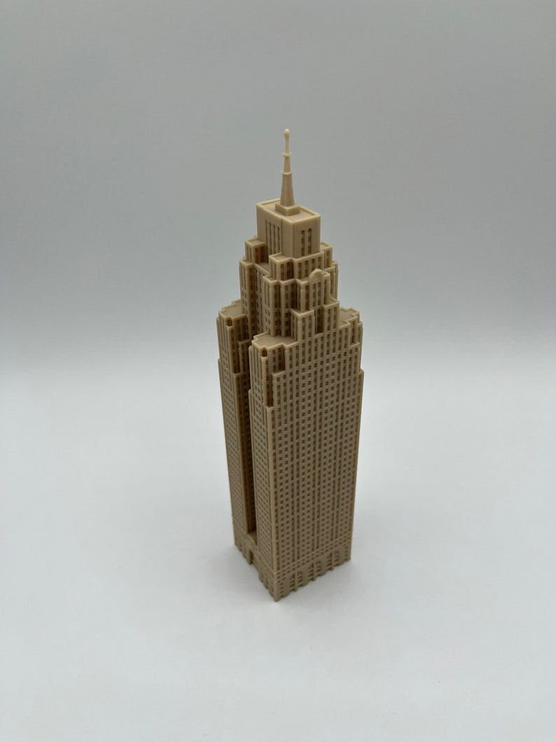 May include: A beige miniature model of a skyscraper with a pointed roof and many windows.