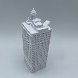 Op de afbeelding: Een wit 3D-geprint model van een hoog gebouw met een koepelvormig dak. Het gebouw heeft veel ramen en is gedetailleerd met architectonische kenmerken.
