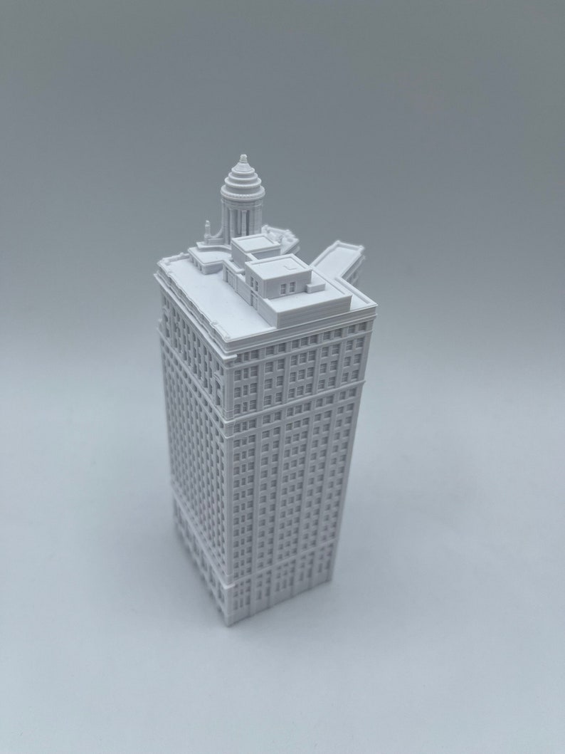 Op de afbeelding: Een wit 3D-geprint model van een hoog gebouw met een koepelvormig dak. Het gebouw heeft veel ramen en is gedetailleerd met architectonische kenmerken.