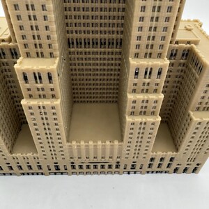 Może przedstawiać: Beżowy model architektoniczny wieżowca, z detalami okien i fasady. Model posiada wiele wież i wklęsłą centralną część. Powierzchnia jest teksturowana.
