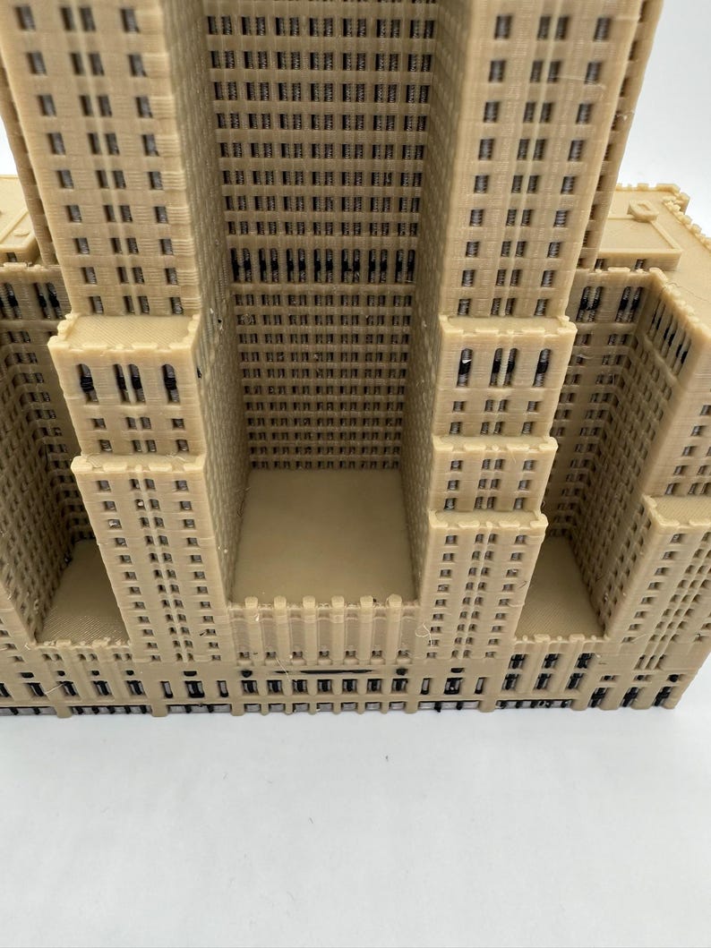 Może przedstawiać: Beżowy model architektoniczny wieżowca, z detalami okien i fasady. Model posiada wiele wież i wklęsłą centralną część. Powierzchnia jest teksturowana.