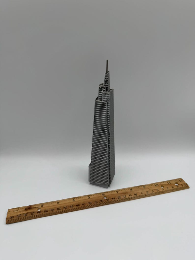 May include: A gray miniature skyscraper model with a ruler. The building has a detailed facade with many windows. The wooden ruler is marked with inch measurements from 1 to 30.