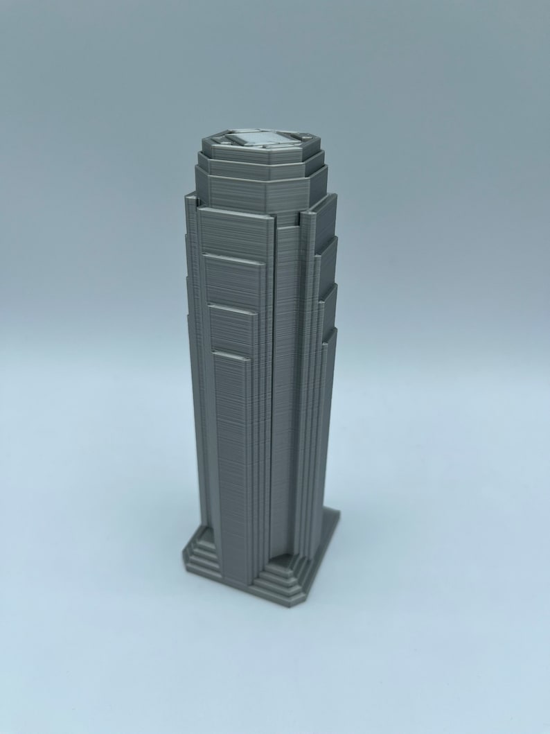 May include: A 3D printed model of a tall, gray skyscraper with a stepped design. The model is made of a smooth, gray plastic and has a detailed facade.