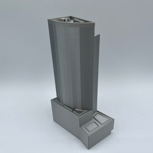 May include: A gray 3D printed model of a tall building with a rectangular base. The building has a curved facade with horizontal lines.