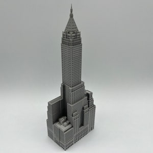 May include: A grey 3D printed model of a skyscraper with a pointed roof and many windows.