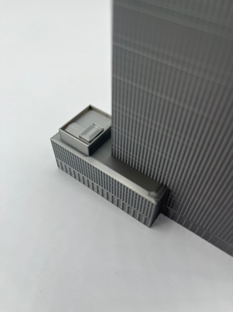 May include: A gray 3D printed model of a skyscraper with a small rooftop addition.