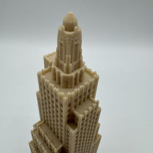 May include: A beige-colored architectural model of a skyscraper. The model features detailed windows and a tiered design, with a domed top. The building's facade has a textured appearance, suggesting a 3D-printed or carved construction.
