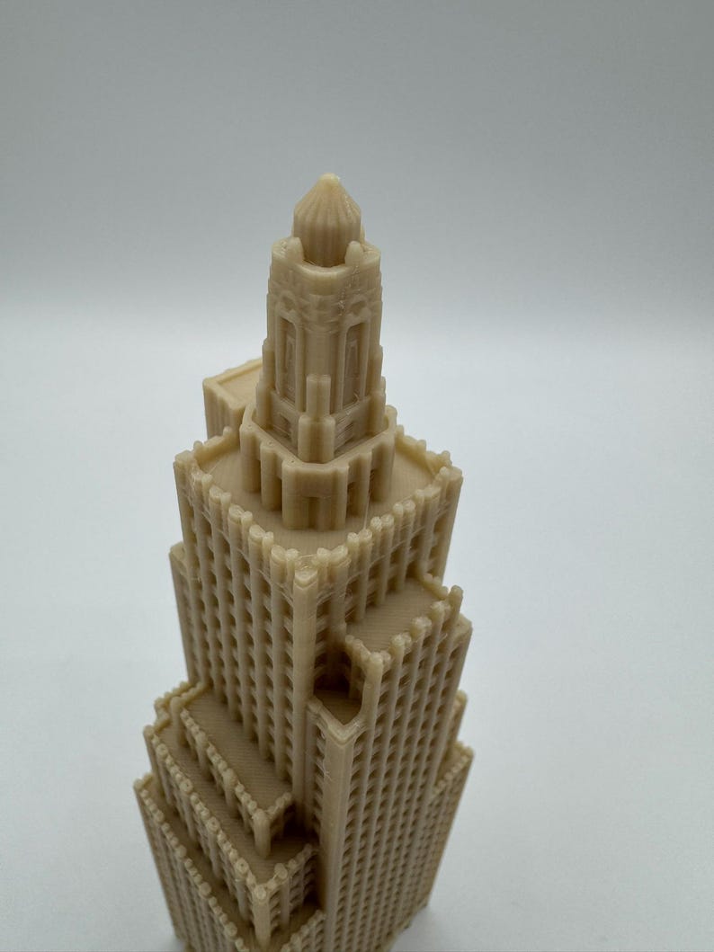 May include: A beige-colored architectural model of a skyscraper. The model features detailed windows and a tiered design, with a domed top. The building's facade has a textured appearance, suggesting a 3D-printed or carved construction.
