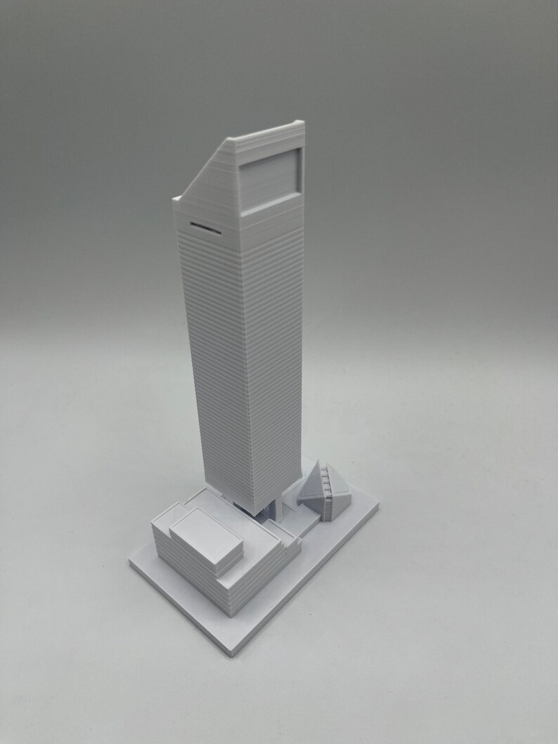 May include: A white 3D printed model of a skyscraper with a smaller building in front of it.