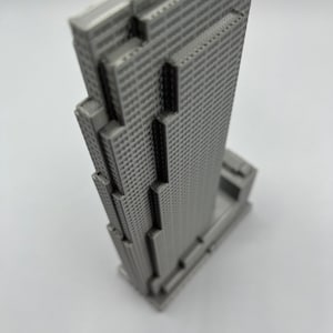 May include: A gray 3D printed model of a skyscraper building.