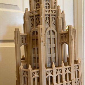 May include: A detailed 3D printed model of a tall building with intricate architectural details, including pointed spires, arches, and windows. The model is made of a light brown plastic and appears to be a replica of a historic skyscraper.