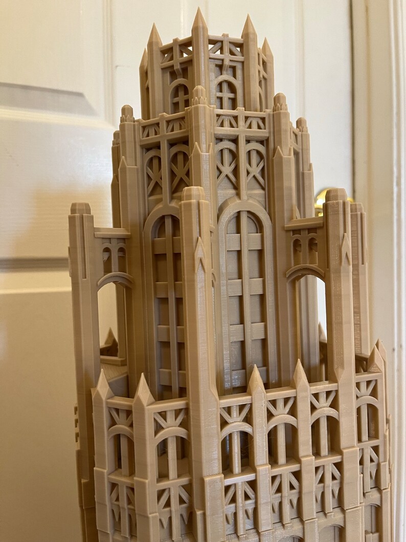 May include: A detailed 3D printed model of a tall building with intricate architectural details, including pointed spires, arches, and windows. The model is made of a light brown plastic and appears to be a replica of a historic skyscraper.