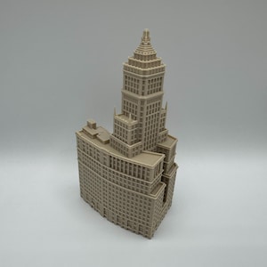Peut inclure: Une maquette architecturale tridimensionnelle beige d'un gratte-ciel présentant une conception en gradins avec une tour centrale, plusieurs niveaux rectangulaires et une grille de petites fenêtres en retrait sur toute la façade.