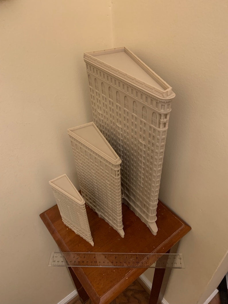 Puede incluir: Tres modelos en miniatura del Flatiron Building de la ciudad de Nueva York, hechos de pl&aacute;stico beige. Los modelos est&aacute;n dispuestos en fila, con el modelo m&aacute;s grande en la parte posterior y el modelo m&aacute;s peque&ntilde;o en la parte delantera. Los modelos est&aacute;n sentados en una mesa de madera.