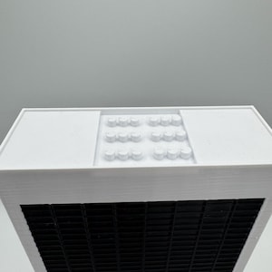 May include: White building model with a black grid pattern on the front and a white roof with a pattern of small white circles.