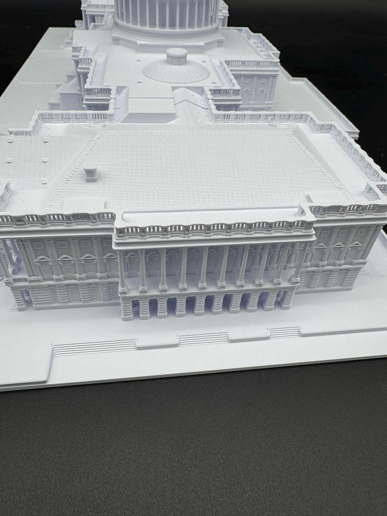 K&ouml;nnte beinhalten: Ein detailliertes, wei&szlig;es 3D-gedrucktes Modell eines Geb&auml;udes mit Kuppel, S&auml;ulen und mehreren Ebenen. Das Modell zeigt architektonische Merkmale, darunter ein Kuppeldach, Balkone und aufwendige Details. Das Modell ist vor einem dunklen Hintergrund platziert.