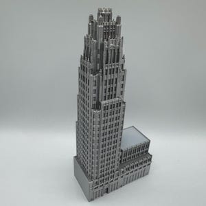 May include: A detailed, gray miniature of a skyscraper with a tall, ornate top. The building has many windows and architectural details, and a smaller, rectangular section at its base.