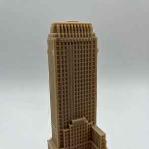 May include: A beige 3D printed model of a skyscraper with a detailed facade and multiple windows.