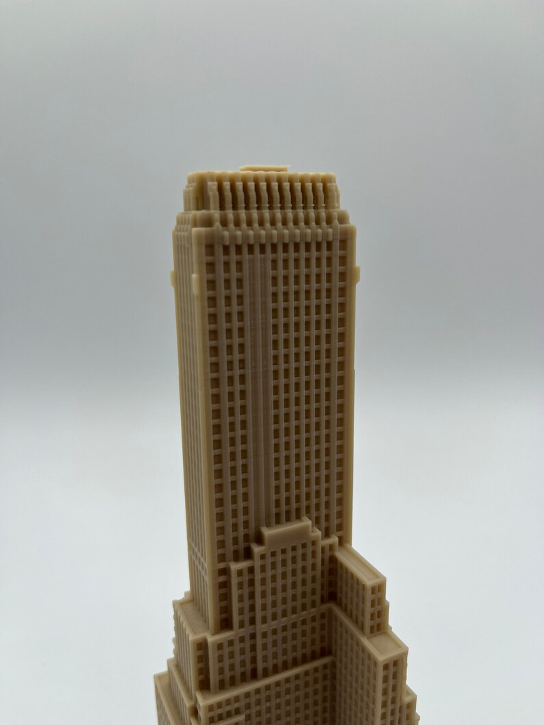 May include: A beige 3D printed model of a skyscraper with a detailed facade and multiple windows.
