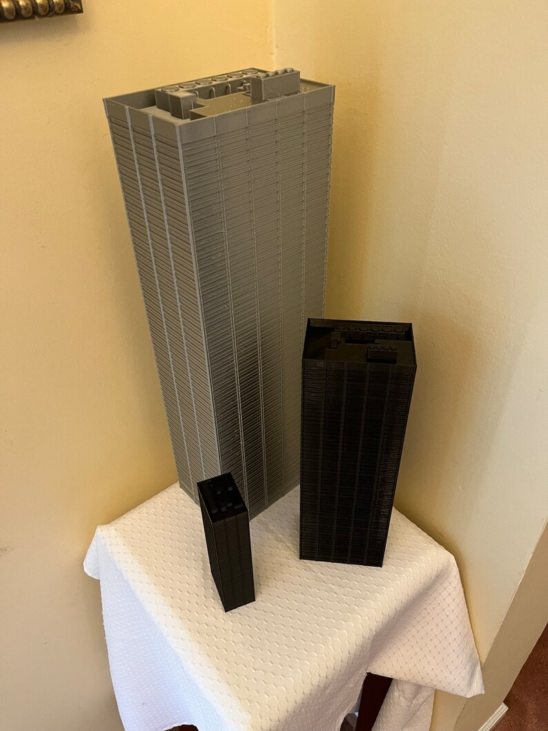 May include: Three miniature skyscrapers made of gray and black plastic blocks. The tallest skyscraper is gray and the two smaller skyscrapers are black.