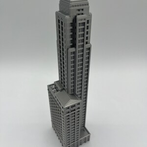 May include: A gray 3D printed model of a tall skyscraper building with many windows and a flat roof.
