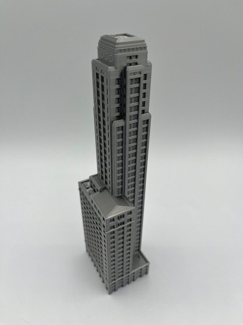 May include: A gray 3D printed model of a tall skyscraper building with many windows and a flat roof.