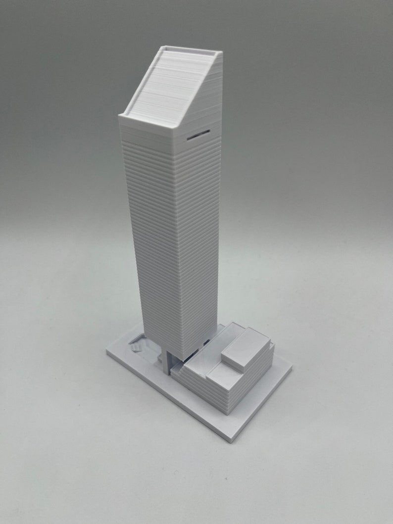 May include: A white 3D printed model of a skyscraper with a flat roof and a smaller building at the base.