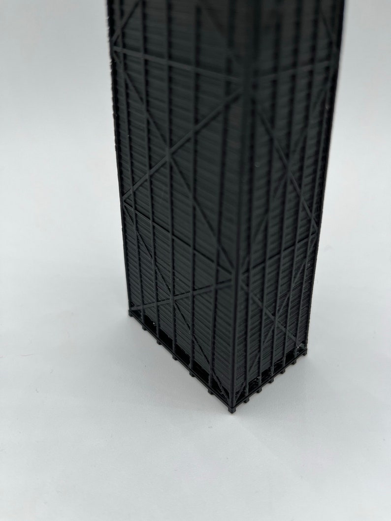 May include: A black, 3D-printed architectural model of a skyscraper. The model features intricate details of the building's facade, including vertical and diagonal support beams. The model is set against a white background.