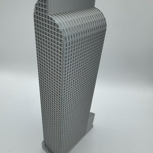 May include: A gray, 3D-printed model of a skyscraper. The building has a rectangular shape with a grid-like pattern on the facade. The top of the building has a curved design, and it sits on a rectangular base.