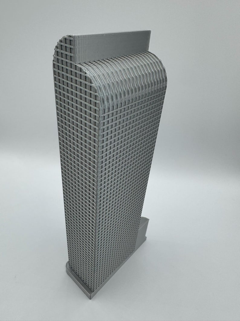 May include: A gray, 3D-printed model of a skyscraper. The building has a rectangular shape with a grid-like pattern on the facade. The top of the building has a curved design, and it sits on a rectangular base.