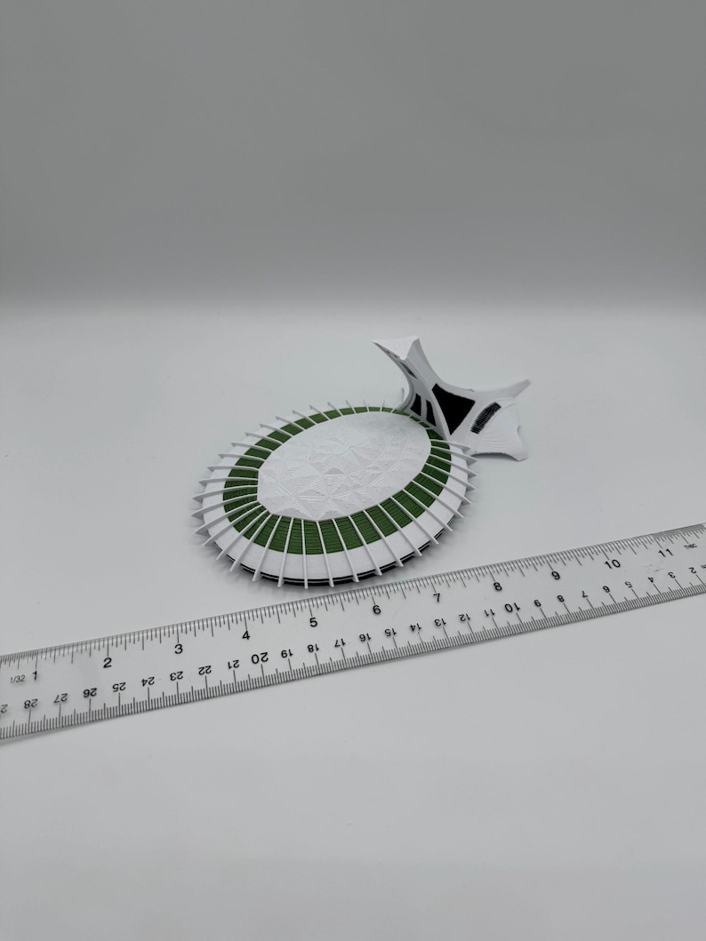 Puede incluir: Maqueta de papel blanca y verde de un estadio, con una regla al lado. El modelo del estadio tiene forma circular con detalles blancos y verdes. La regla est&aacute; marcada con cent&iacute;metros.