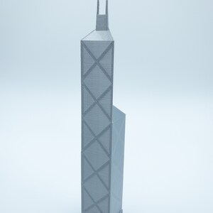 May include: A gray 3D-printed model of a skyscraper. The building has a rectangular shape with a distinctive cross-braced facade. The model includes architectural details such as a base and a spire at the top. The model is approximately 12 inches tall.