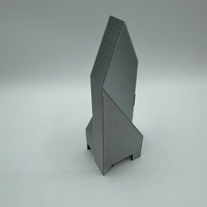 May include: A gray 3D printed model of a tall, pointed building with a geometric design.