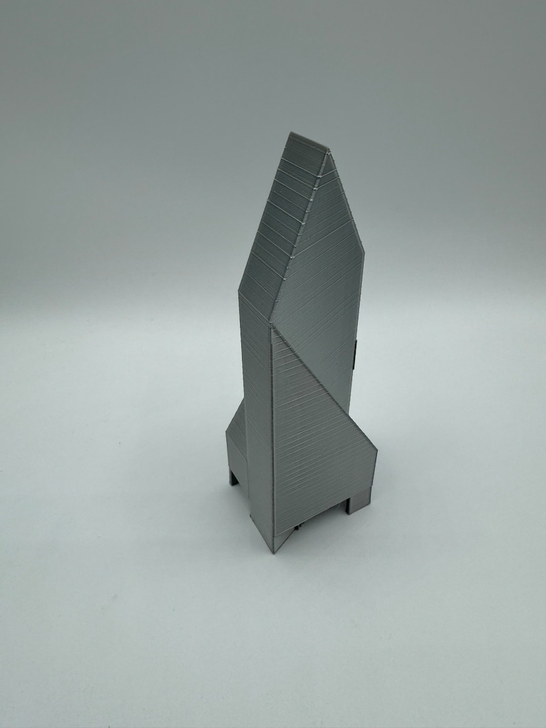 May include: A gray 3D printed model of a tall, pointed building with a geometric design.