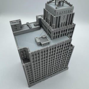 May include: A gray, 3D-printed model of a skyscraper with the word "EASTERN" on the top. The building has a detailed facade with many windows and architectural features. The model is set against a plain white background.