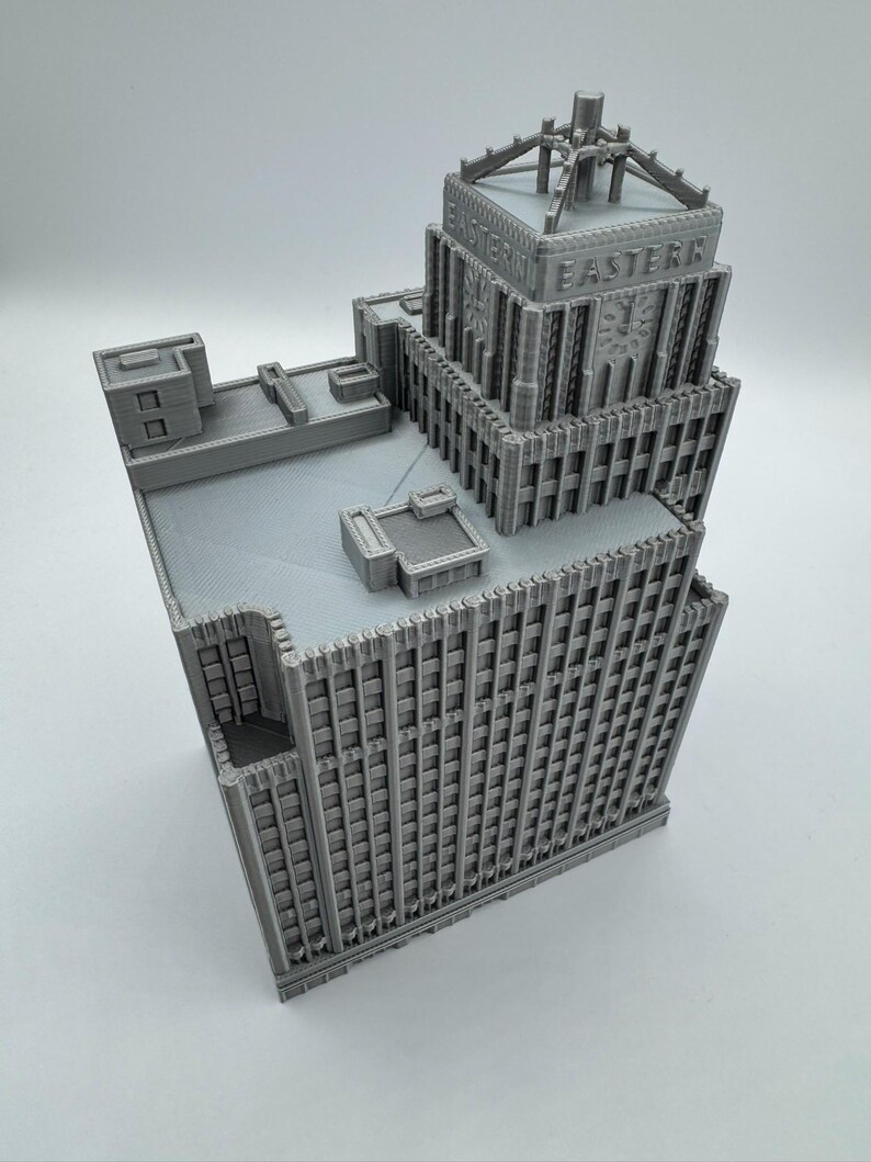 May include: A gray, 3D-printed model of a skyscraper with the word "EASTERN" on the top. The building has a detailed facade with many windows and architectural features. The model is set against a plain white background.