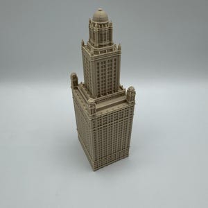May include: A beige architectural model of a tall building with a detailed facade. The model features a rectangular base, a multi-tiered structure, and a domed top. The building has many windows and decorative elements.