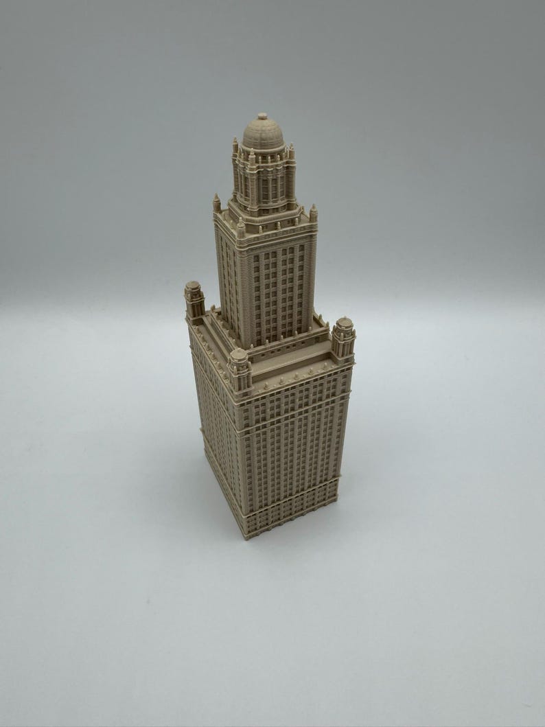 May include: A beige architectural model of a tall building with a detailed facade. The model features a rectangular base, a multi-tiered structure, and a domed top. The building has many windows and decorative elements.