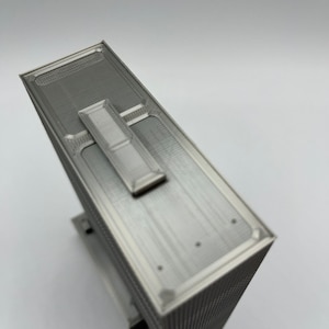 May include: A silver-colored 3D printed model of a skyscraper with a flat roof and a small rectangular structure on top.