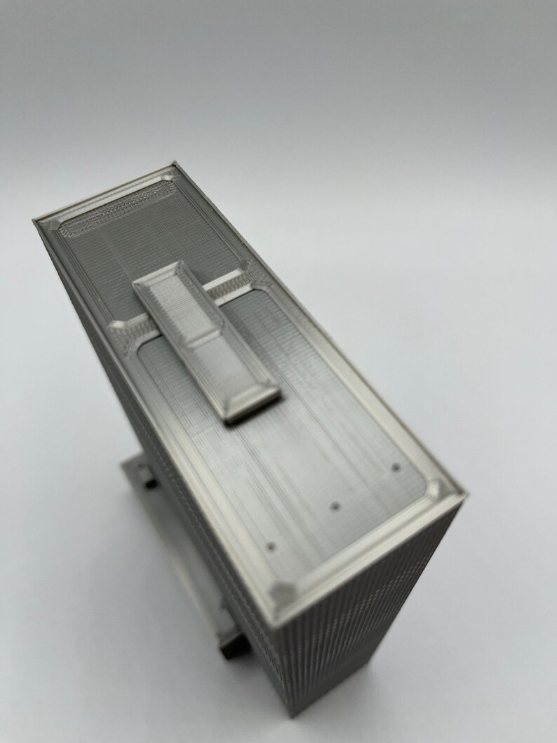 May include: A silver-colored 3D printed model of a skyscraper with a flat roof and a small rectangular structure on top.