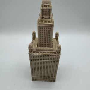 May include: A beige architectural model of a tall building with a detailed facade. The model features a rectangular base with a tower that has a domed top. The building has many windows and decorative elements.