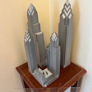 May include: A 3D printed model of the Philadelphia skyline, featuring three buildings in a gray color. The model is displayed on a wooden table.