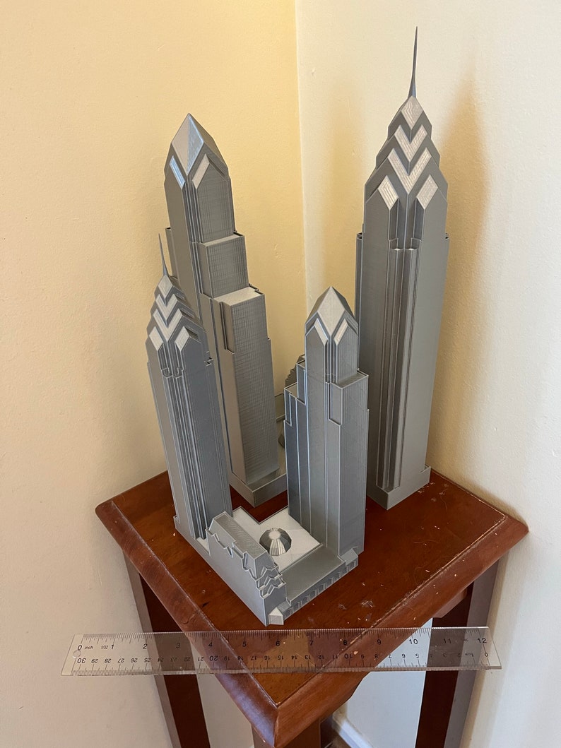 May include: A 3D printed model of the Philadelphia skyline, featuring three buildings in a gray color. The model is displayed on a wooden table.
