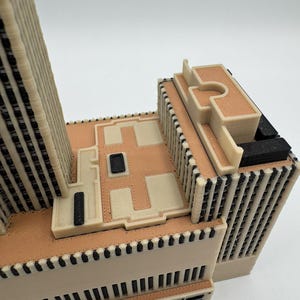 Puede incluir: Maqueta arquitect&oacute;nica detallada de un edificio, con una combinaci&oacute;n de colores beige y negro. El modelo presenta detalles intrincados, incluyendo l&iacute;neas verticales y patrones rectangulares, con un techo plano y m&uacute;ltiples niveles. El dise&ntilde;o es moderno y geom&eacute;trico.