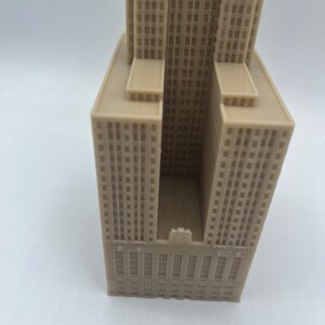 May include: A beige 3D printed model of a skyscraper with a clock face on the front.