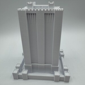 May include: White 3D printed model of a tall tower with crenellations and a square base.