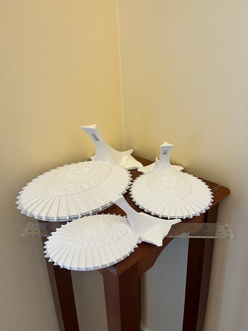 May include: Three white ceramic cake stands with a scalloped edge and a raised center. The stands are stacked on top of each other on a wooden table.