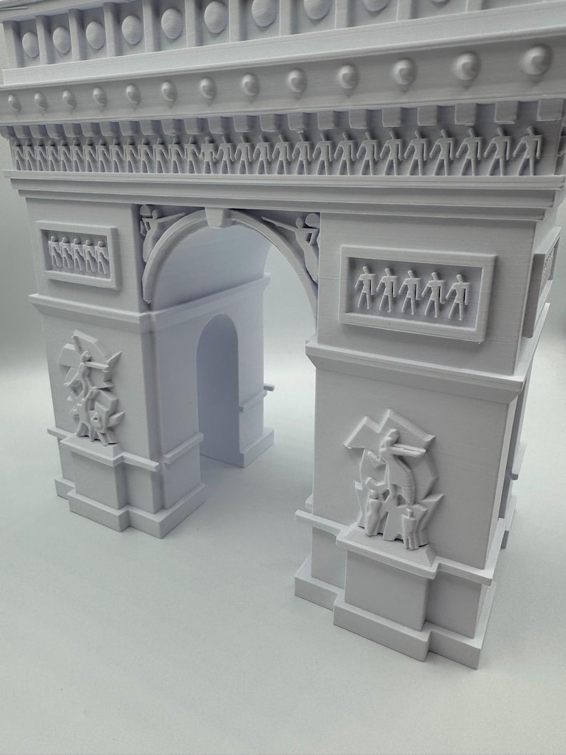 Może przedstawiać: Jasnoszara miniaturowa replika Łuku Triumfalnego. Model architektoniczny zawiera szczeg&oacute;łowe rzeźby, w tym figury i elementy dekoracyjne. Łuk jest klasycznym pomnikiem.