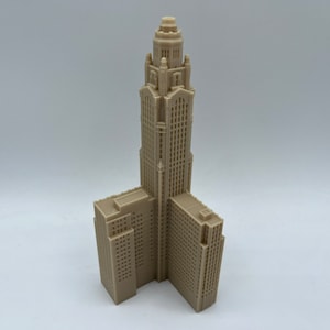 May include: A beige 3D printed model of a skyscraper with a tall, narrow tower and two shorter wings.