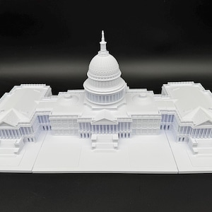 K&ouml;nnte beinhalten: Ein wei&szlig;es Architekturmodell des US-Kapitolgeb&auml;udes. Das Modell ist sehr detailliert und zeigt die Kuppel, die S&auml;ulen und die Gesamtstruktur. Es besteht aus einem wei&szlig;en Material und steht auf einer flachen Oberfl&auml;che.